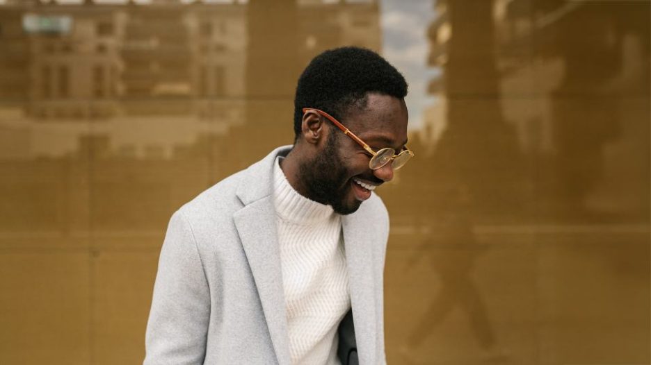 young bearded male manager in smart casual outfit smiling brightly on street against building with glass walls