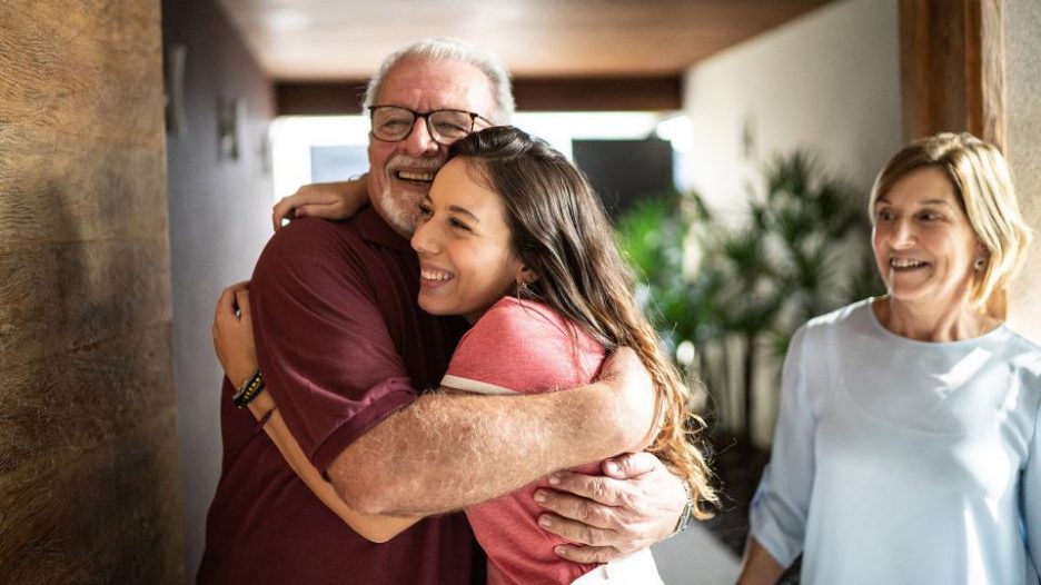 Young woman hugging her father with her mother looks on happily