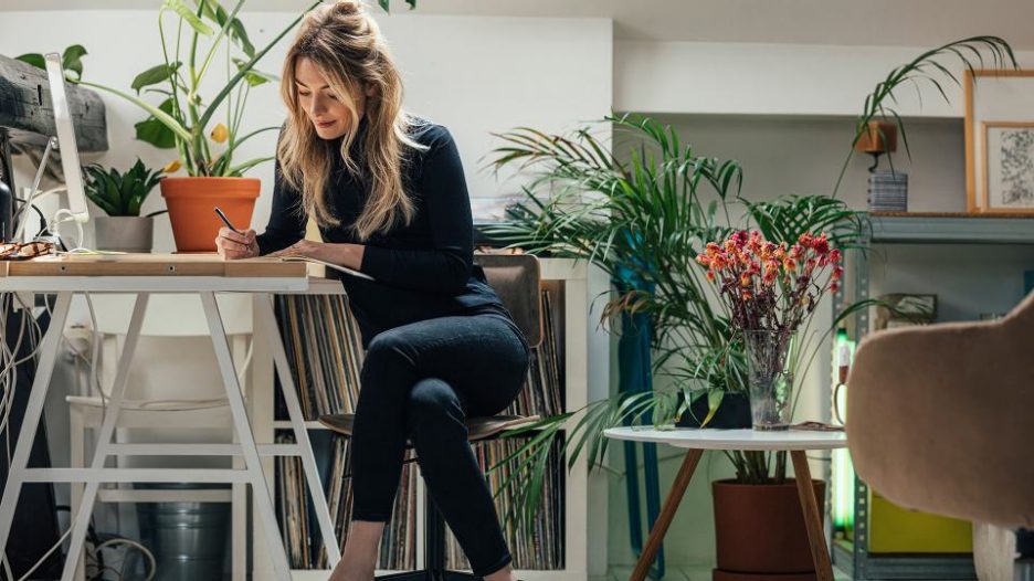 Woman writing in a notebook while sitting at a table in her bohemian styled home