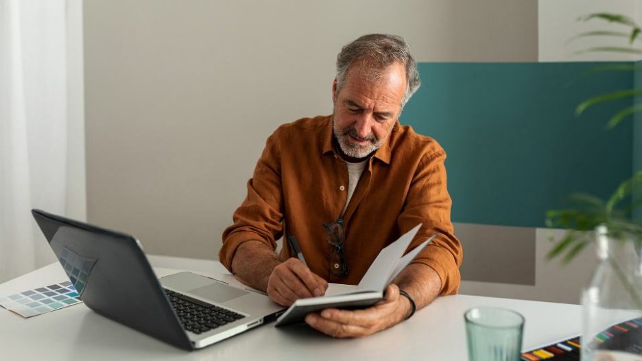 mature man smiling working writing in his notebook sitting at a desk