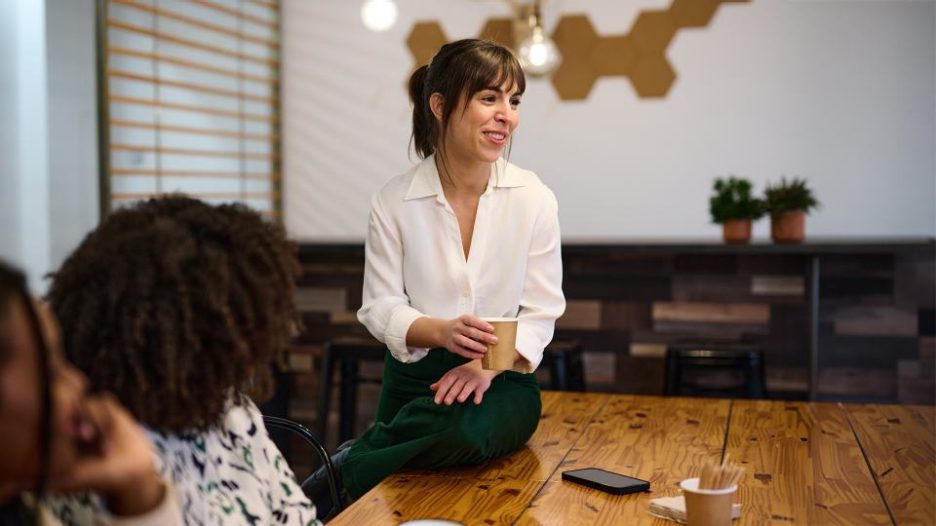 A businesswoman with a bright smile participates in a team meeting, holding a coffee cup, in a contemporary office space