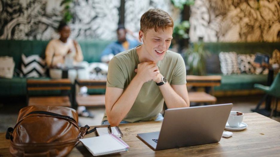 Young man using his laptop with earbuds at a cafe 