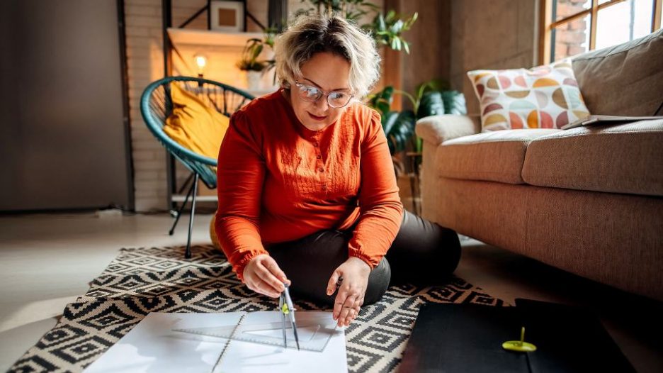 Woman in glasses using a map and compass while sitting on the floor of her home