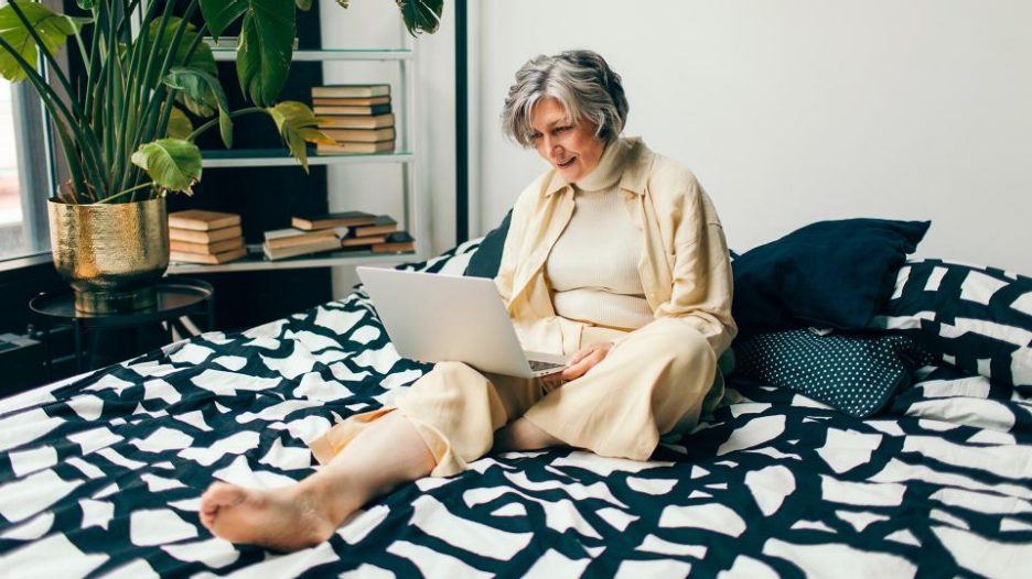 a mature lady relaxing on her bed on her laptop