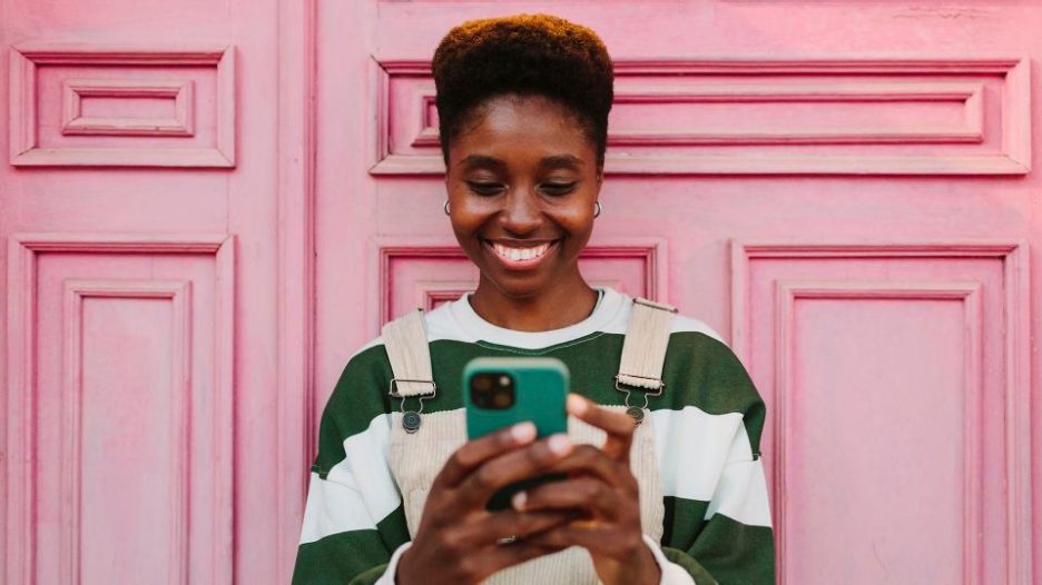 woman typing on a smartphone sitting against a bright pink door