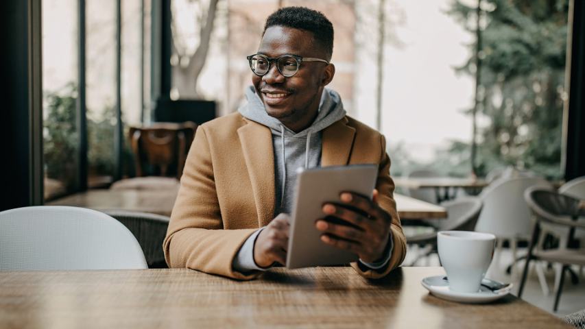 Smiling male holding tablet while sitting in coffee shop