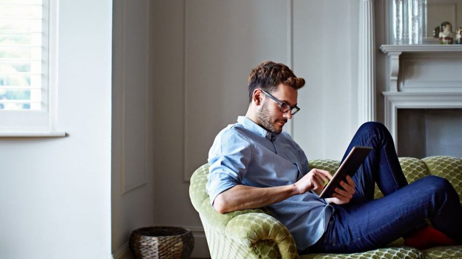 Man with glasses in a blue shirt is using his phone while sitting on a green sofa