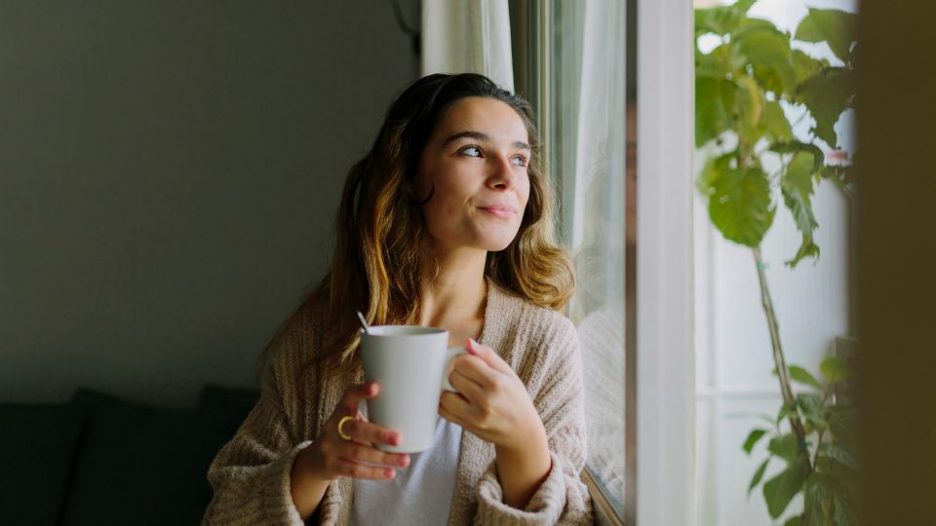 a woman is looking through a window with a coffee mug in her hands