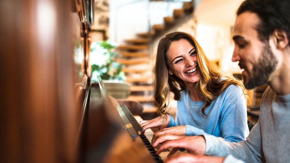 Smiling happy couple playing an upright piano together
