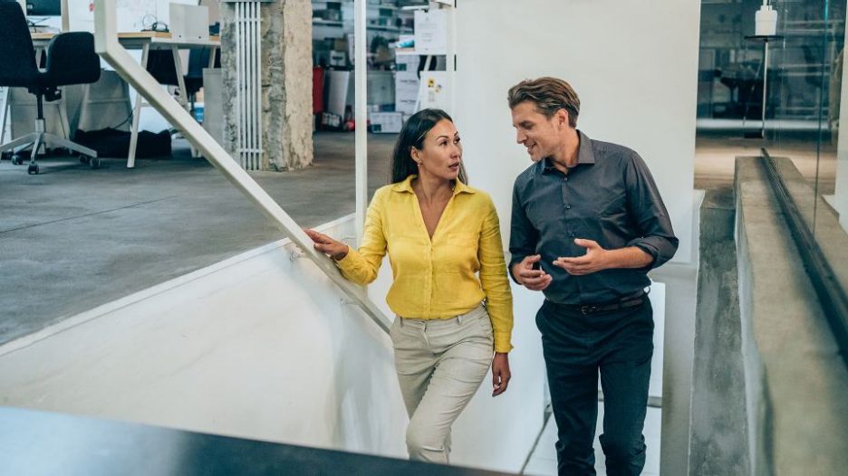 Two colleagues discussing while walking up the stairs in a modern office 1368665540
