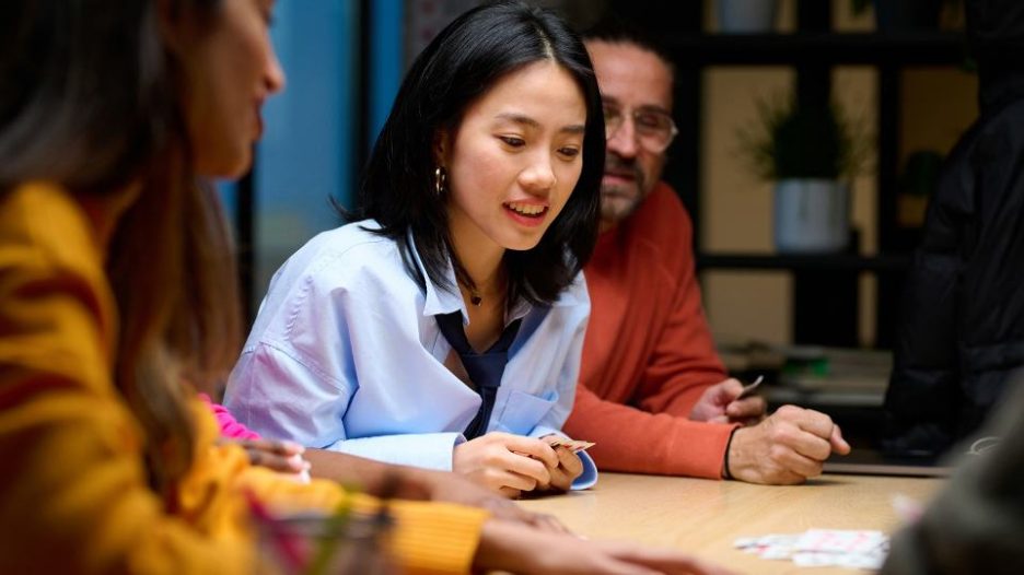 smiling woman looking at pile of cards on the table while playing with her colleagues