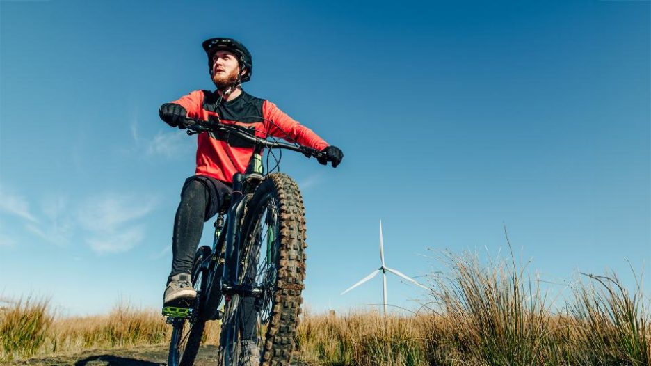 young man mountain biking in field with a wind turbine in the background.
