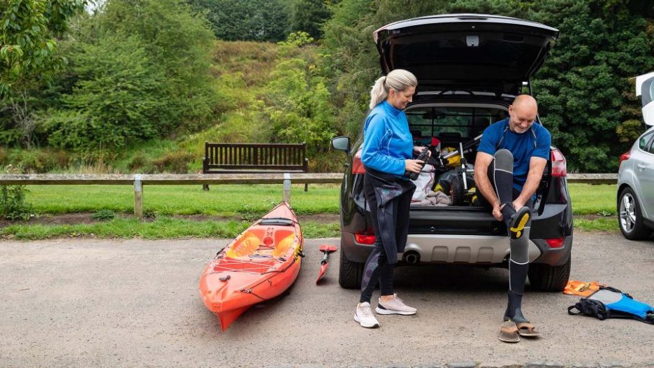 Sporty mature couple are getting ready for kayaking with their car and sports equipment
